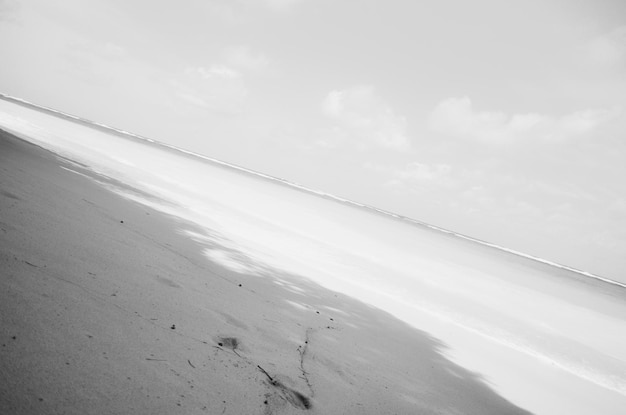 a black and white photo of a beach with a few clouds in the background