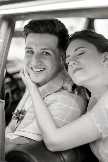 Black and white photo of beautiful young bride and smiling handsome groom in the retro car