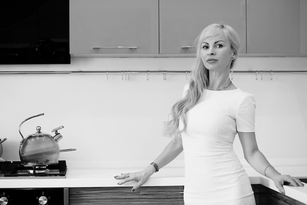 Black and white photo of blonde girl posing on camera standing in kitchen