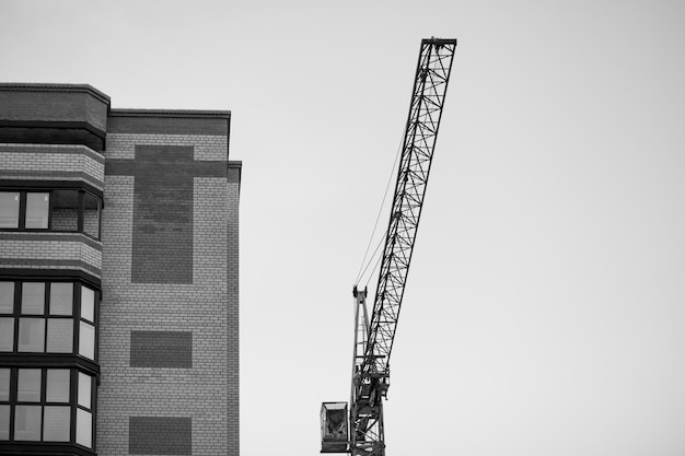 A black and white photo of a crane next to a building.