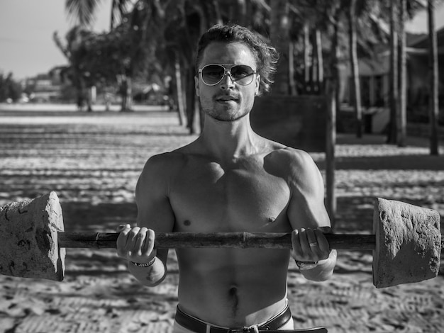 Black and white photo of fitness man with barbell on the beach