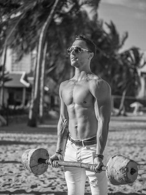 Black and white photo of fitness man with barbell on the beach