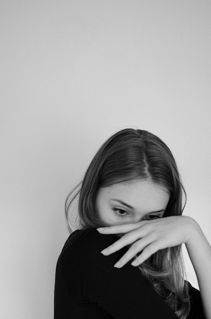 Black and white photo of a girl on a plain backround hiding behind her palm