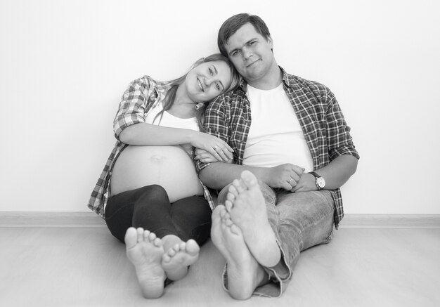 Black and white photo of happy pregnant couple hugging on floor