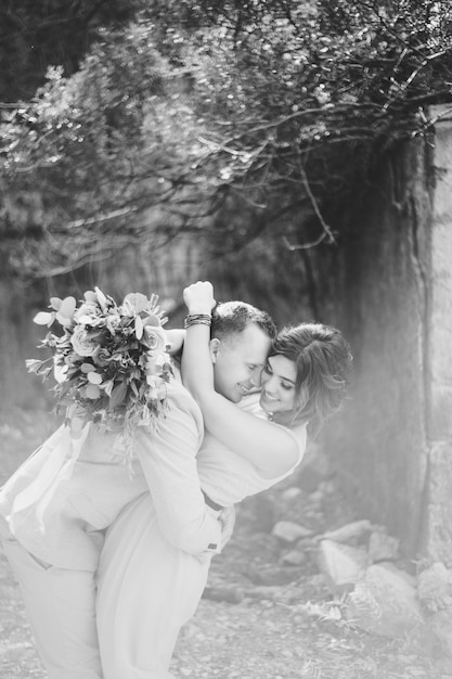Black and white photo happy smiling groom hugs bride in a lovely dress bride holds in her hands a