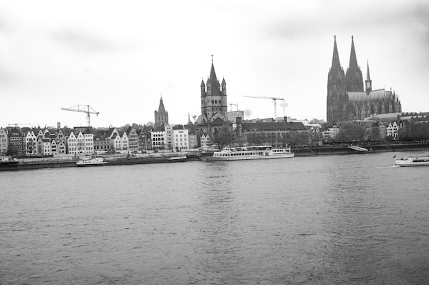 A black and white photo of a river with cologne cathedrals in the background.