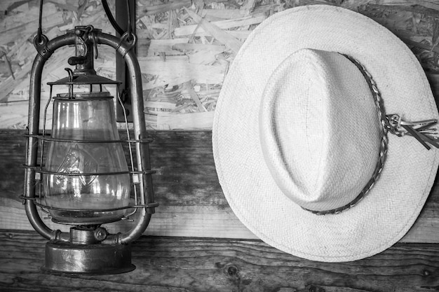 Black and white photo on the wooden wall hangs white cowboy hat and old lamp in cowboy house