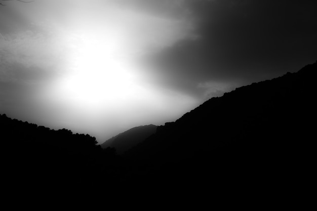 Black and white photograph of the silhouette of a mountain with clouds in the sky minimalist