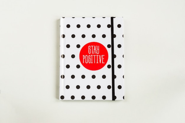 Photo black and white polka dot note book with red circla and stay positive inscription on the cover.