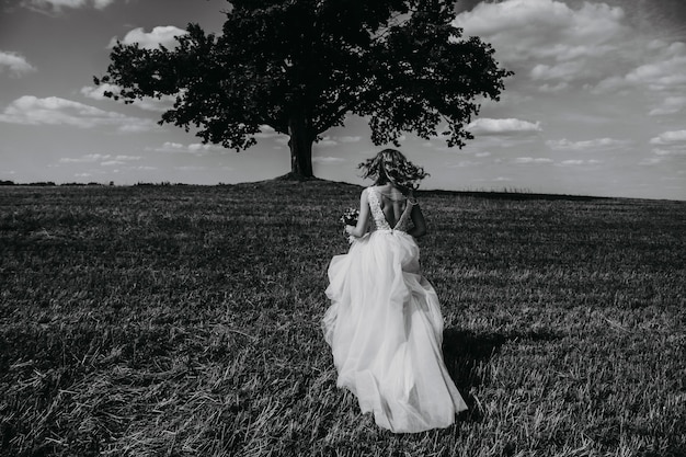 Ritratto bianco e nero di una sposa che corre in un campo.