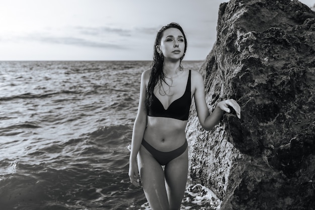 Foto ritratto in bianco e nero di una ragazza sul mare vicino alle pietre al tramonto