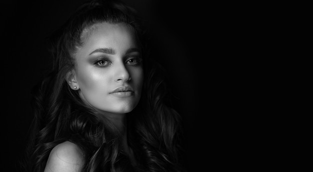 Black and white portrait of a glorious young woman posing in the shadows at studio. Empty space