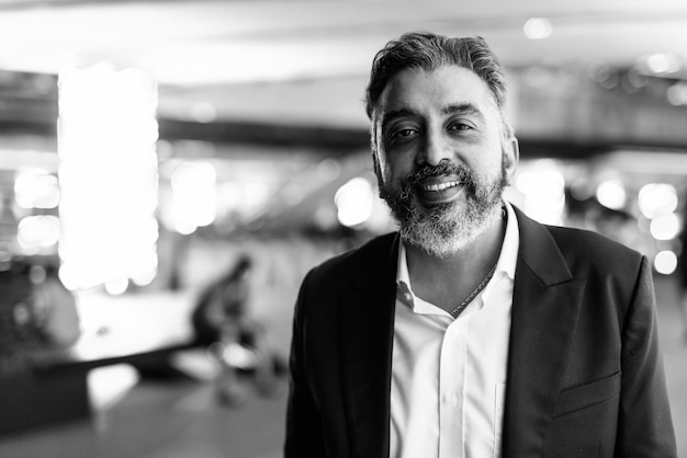 Black and white portrait of handsome Indian businessman in city at night smiling