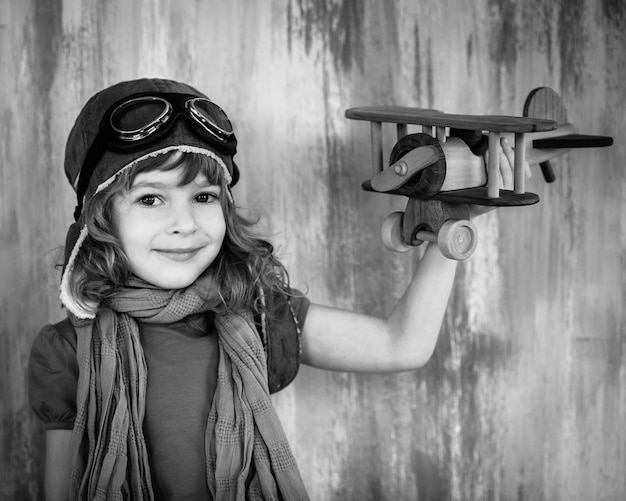 Black and white portrait of happy kid playing with toy wooden airplane indoors