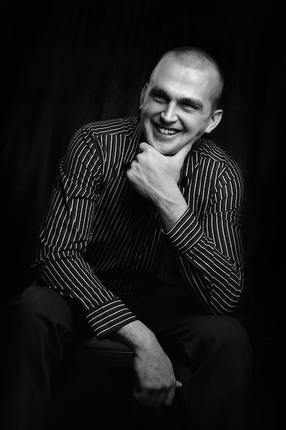 Black and white portrait of a man in the studio sitting with his on the chinlooking on the side