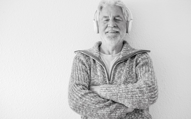 Black and white portrait of senior bearded man with closed eyes isolated on white background listening to music with headphones