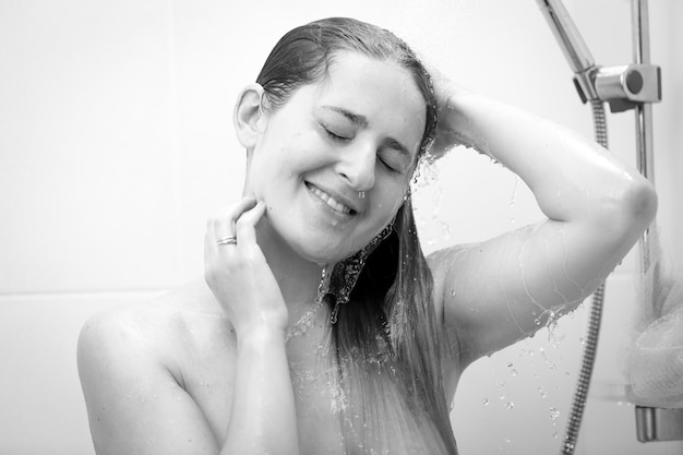 Black and white portrait of smiling woman washing hair at shower