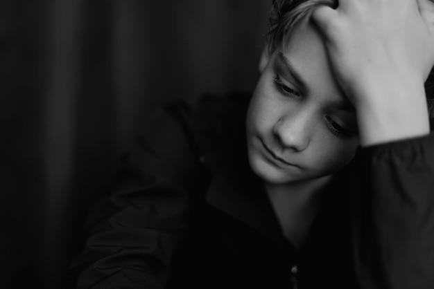 Black and white portrait of teenage boy on dark background Low key close up shot of a young teen boy Black and white photography Selective focus