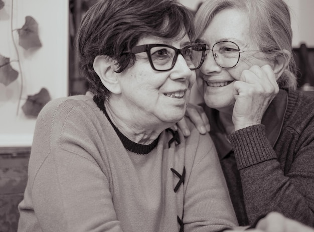 Black and white portrait of two smiling relaxed senior women making confidences sharing secrets