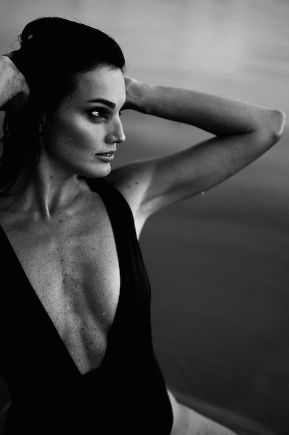 Black White Portrait of Young Woman with Muscular Body in Piece Swimsuit Looking Away. Hands at Head. Girl with Troubled Eye.