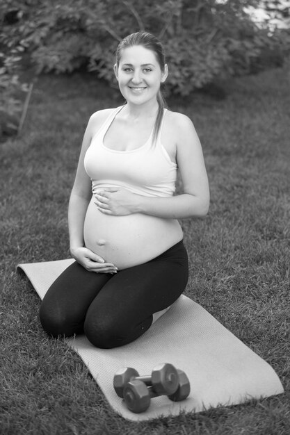 Black and white pregnant woman sitting on knees at park and holding big tummy