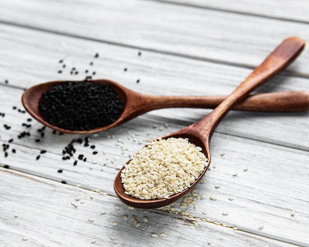 Black and white sesame seeds in a spoons on a wooden table