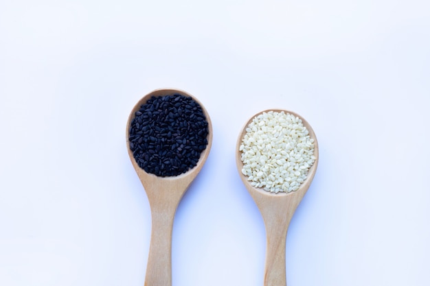 Black and white sesame seeds on wooden spoon, white background. 