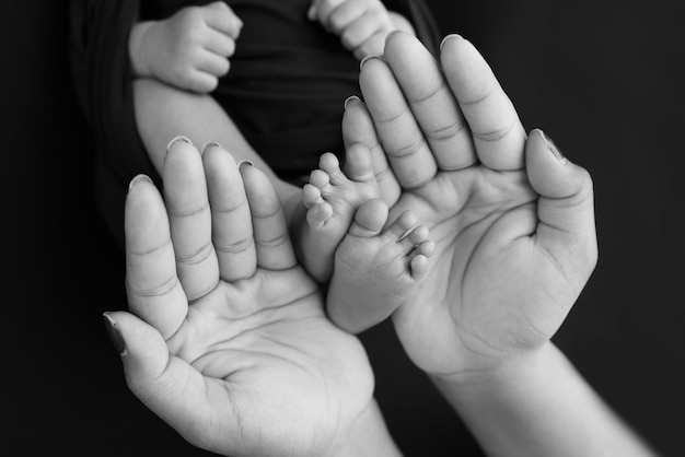 어머니의 검은색과 흰색의 아름다운 모양 손은 사랑의 가족 안전과 조산 개념 또는 NICU 관리를 가진 보호 어린이와 함께 검은 배경에 작은 갓난 아기 발을 잡고 있습니다.