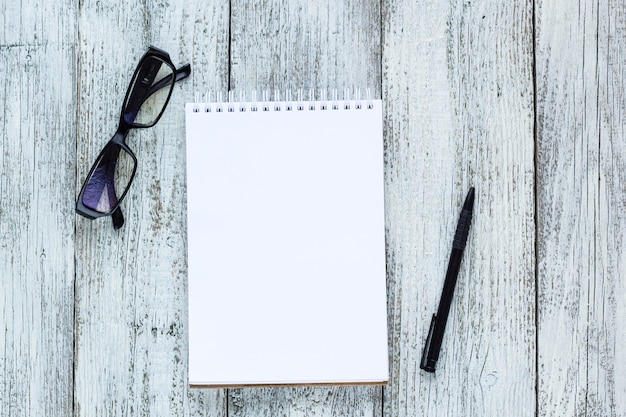 Black and white still life: opened blank notepad, notebooks, pen, glasses.