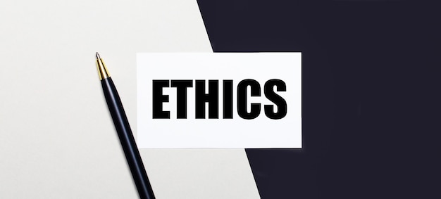 On a black and white surface lies a pen and a white card with the text ETHICS