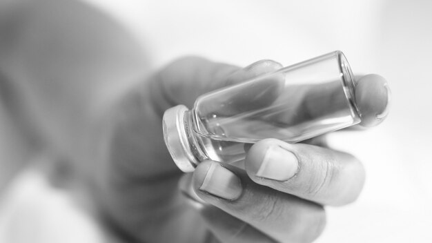 Black and white view of female nurse holding glass vial with medicines.