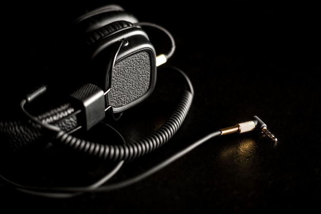 Black wired on ear headphones with gold headphone jack on dark background