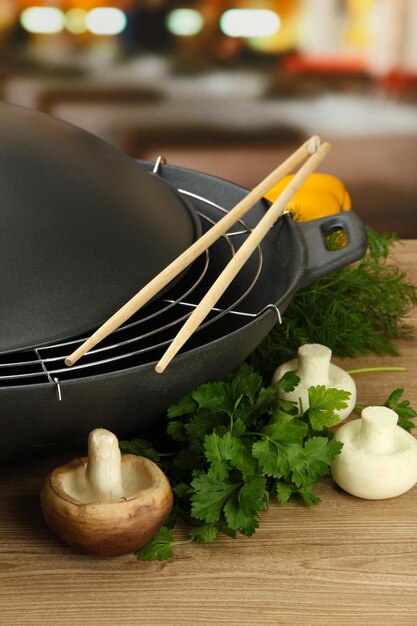Black wok pan and vegetables on kitchen wooden table close up