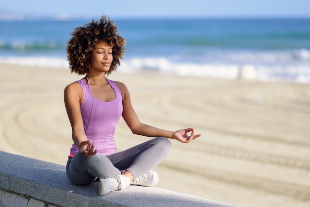 Black woman, afro hairstyle, in lotus asana with eyes closed in the beach