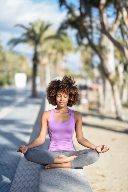 Black woman, afro hairstyle, in lotus pose with eyes closed in the beach