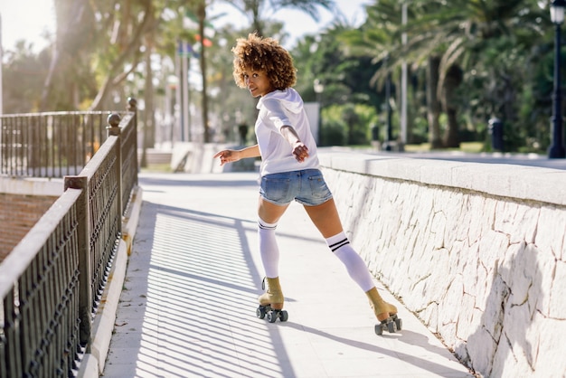 Black woman, afro hairstyle, on roller skates riding near the beach.