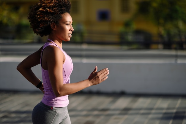 Black woman, afro hairstyle, running outdoors in urban road. 