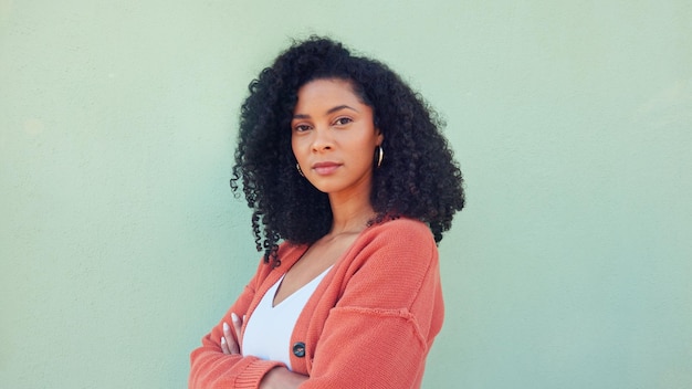 Photo black woman confident beauty and young model pose for portrait with afro hair on green background african girl in orange sweater fold arms with cool serious face and casual fashion lifestyle