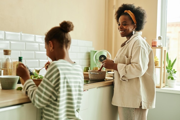 black woman cooking on stove looking at girl with love at kitchen