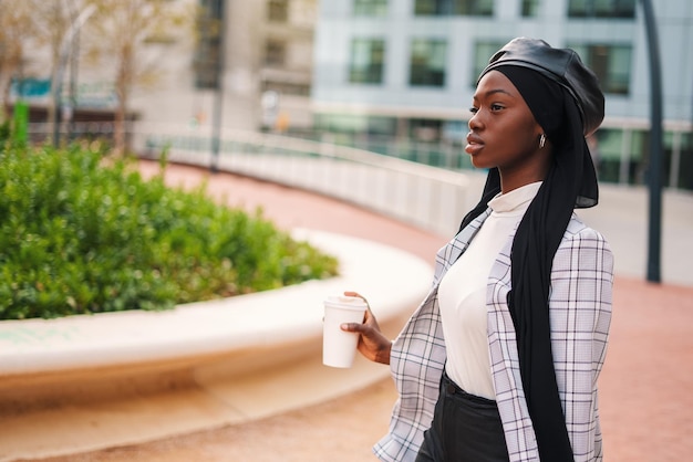 Black woman in headscarf with takeaway beverage in park