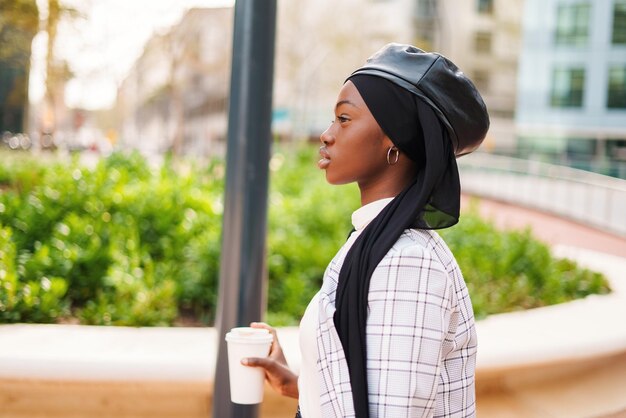 Black woman in headscarf with takeaway beverage in park