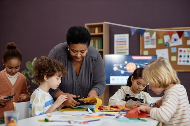 Black woman helping group of little children doing crafts in preschool class