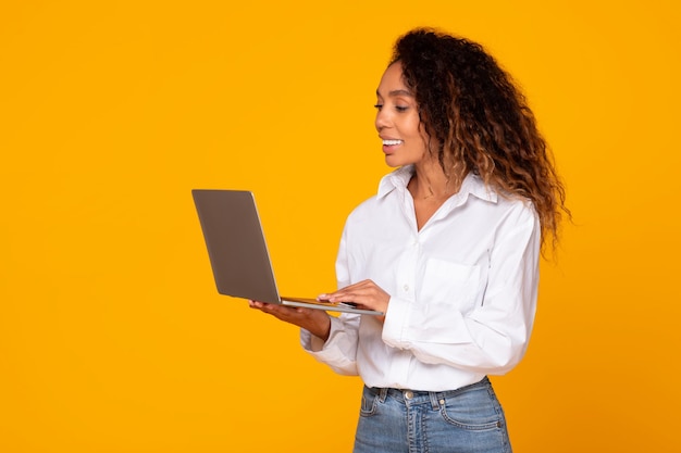 Black woman holding and using laptop working online in studio