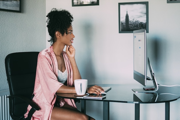 Black woman at home working with computer and coffee in the morning