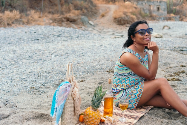 Черная женщина сидит на пляже с бокалом вина на летних каникулах