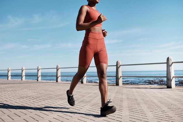 Black woman legs or running by city beach ocean or sea in healthcare workout cardiovascular wellness training or marathon exercise Runner sports athlete or personal trainer on promenade fitness