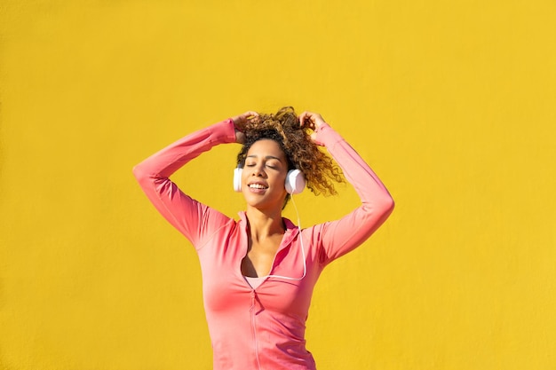 Black woman listening to music on headphones while relaxing on yellow background
