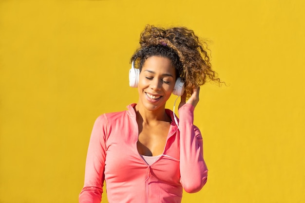 Black woman listening to music on headphones while relaxing on yellow background