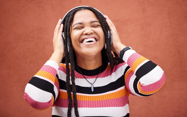 Black woman music headphones and happy by wall in city for walk adventure and me time with smile Young gen z girl audio streaming and excited listening on radio website and happiness in metro