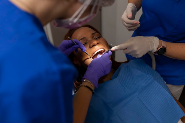 A black woman patient keeps her mouth open while dental hygienist cleans teeth at the dental clinic